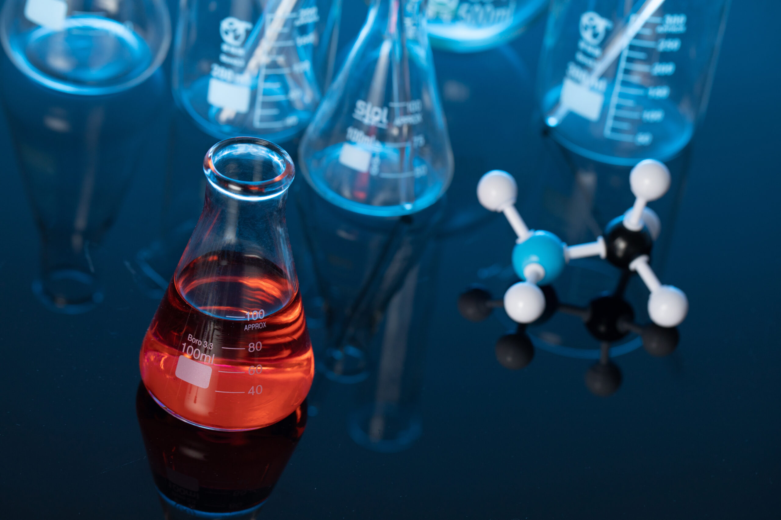 A glass flask with red liquid and a molecule structure on a lab table
